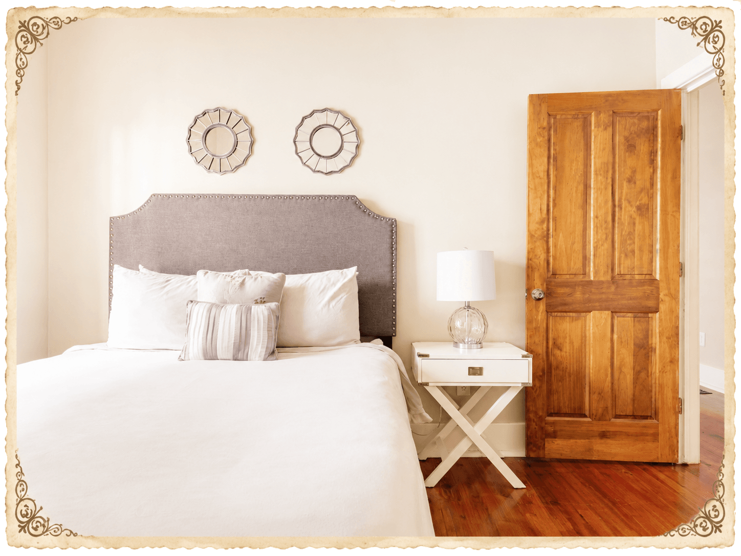 Second bedroom — framed prints above the upholstered headboard, side table, wood door